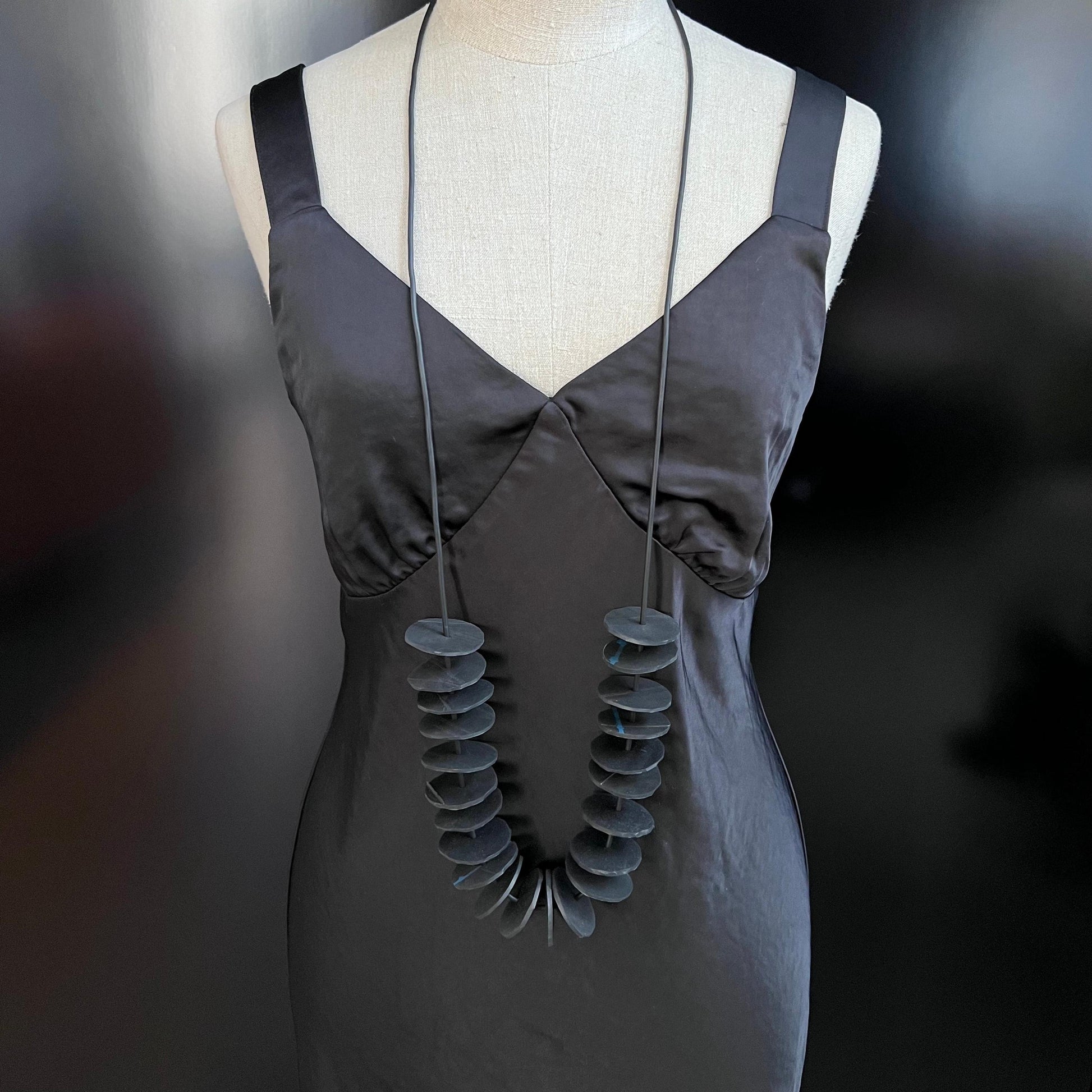 A mannequin wears a necklace with small circles on s strand worn long