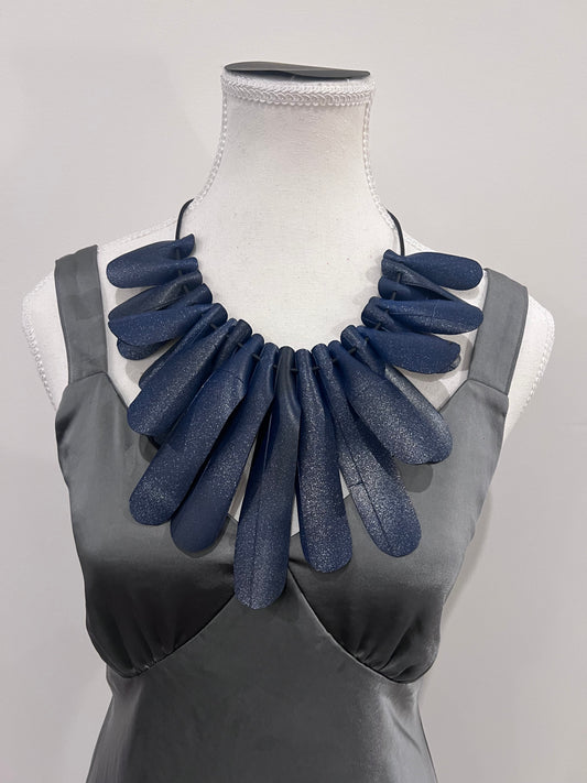 A mannequin wears an elaborate blue sparkly necklace made from bicycle inner tube rubber strands