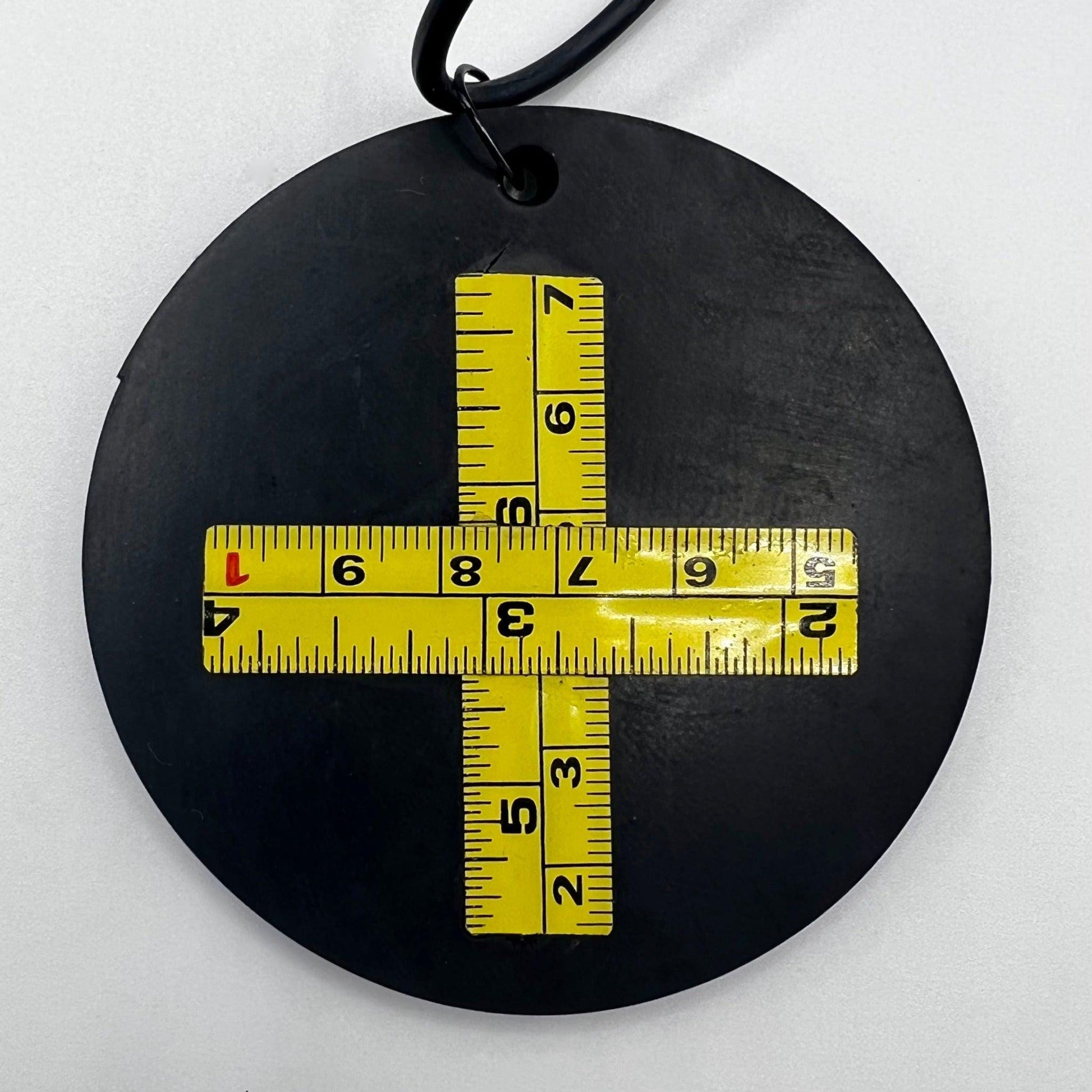 A round rubber necklace pendant overlayed with a cross made from a broken metal tape measure