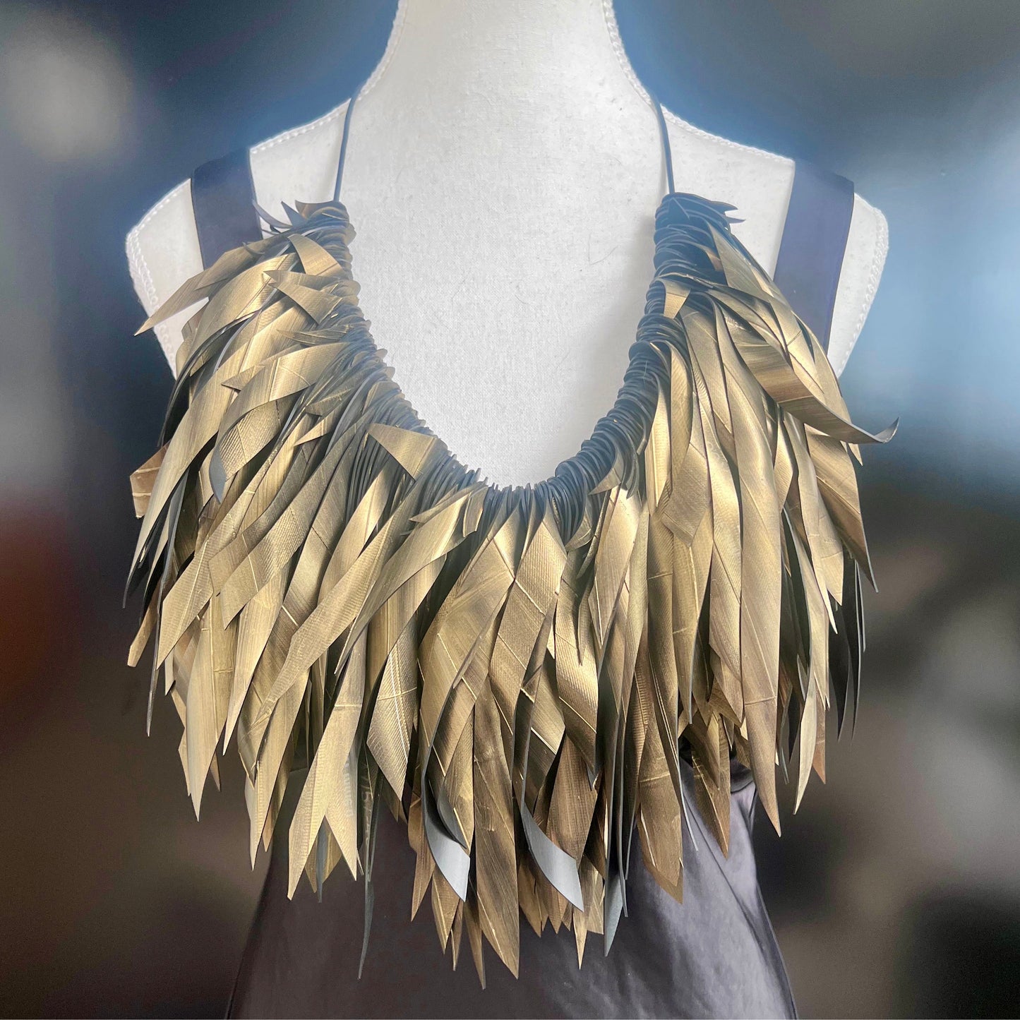 Gold painted recycled rubber necklace on a mannequin against a blurred background
