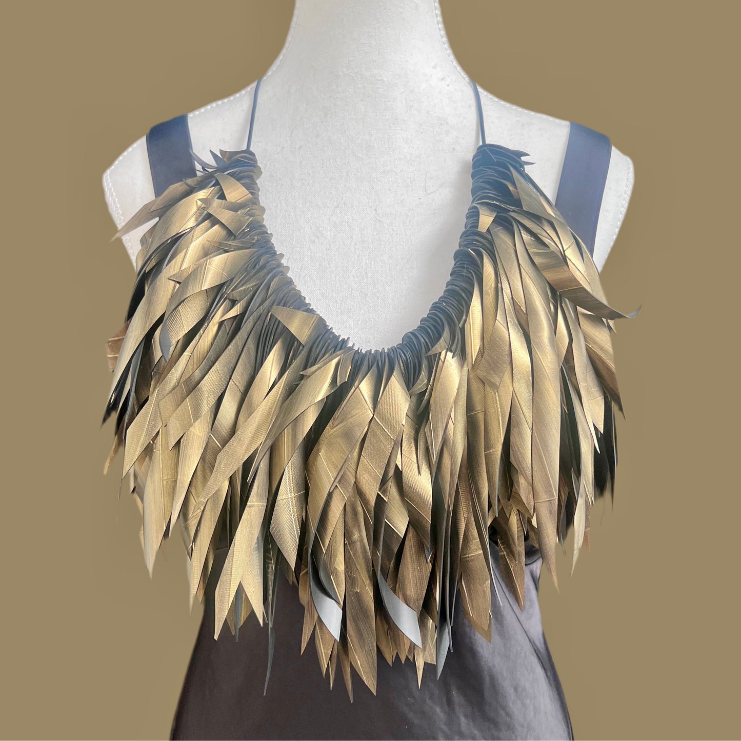 Mannequin wearing a gold feathered necklace on a brown background