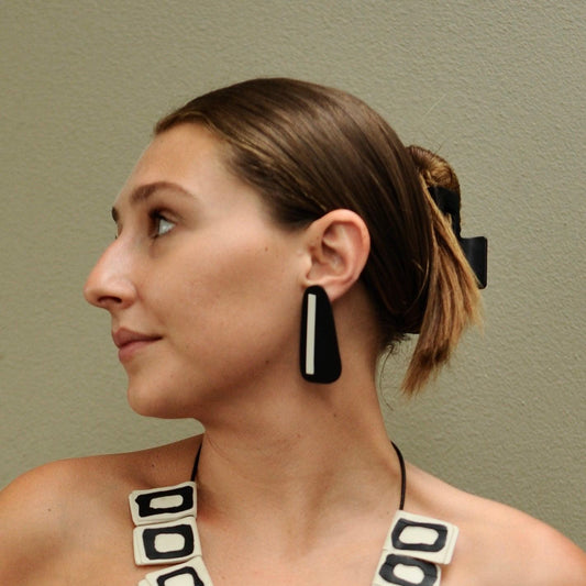A woman wears a long stud earring of black with white stripe