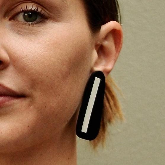A woman wears a long stud earring of black with white stripe