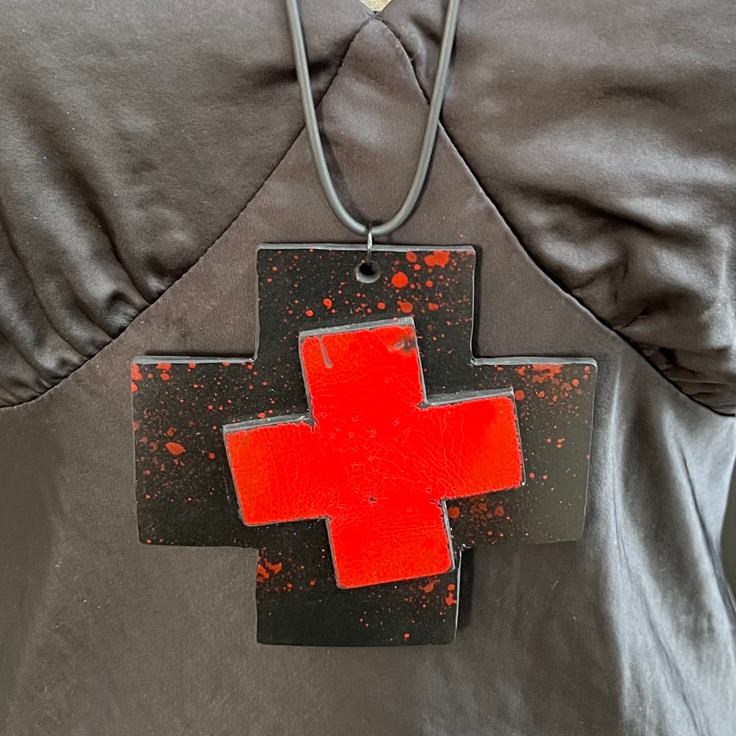 A large rubber cross shaped pendant layered with more rubber and painted in red.