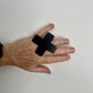 A hand wears a large cross shaped black ring