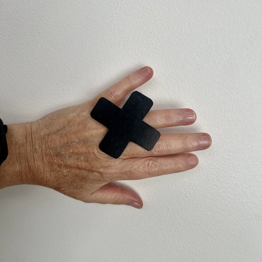 A hand wears a large cross shaped black ring