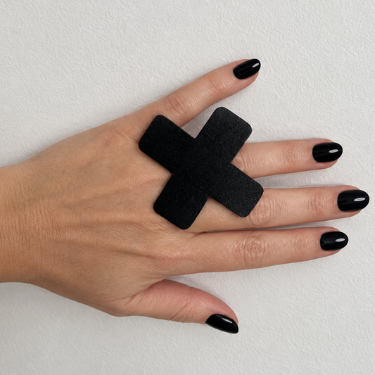 A hand wears a large cross shaped  black ring
