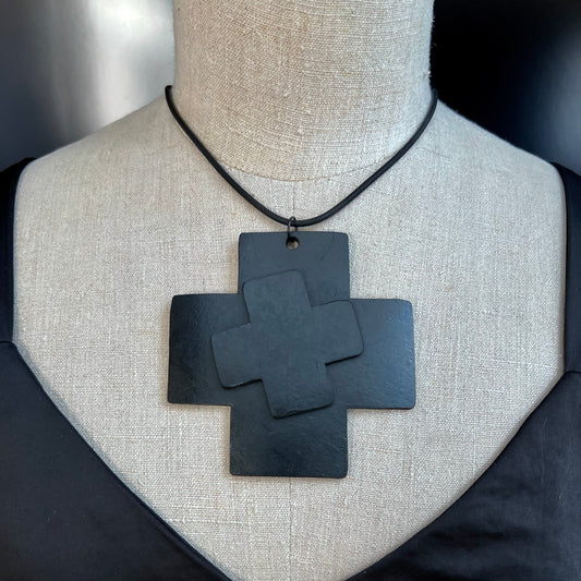 A mannequin wears a large rubber black cross necklace detailed with a smaller angled cross on top