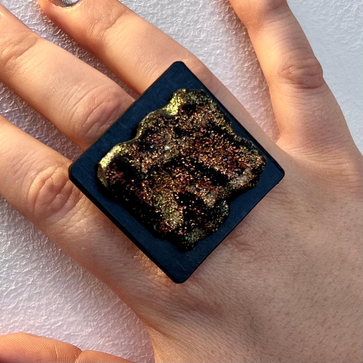 A woman's hand wearing a large rubber black and painted glitter ring