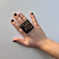A woman's hand wearing a large rubber black and painted glitter ring