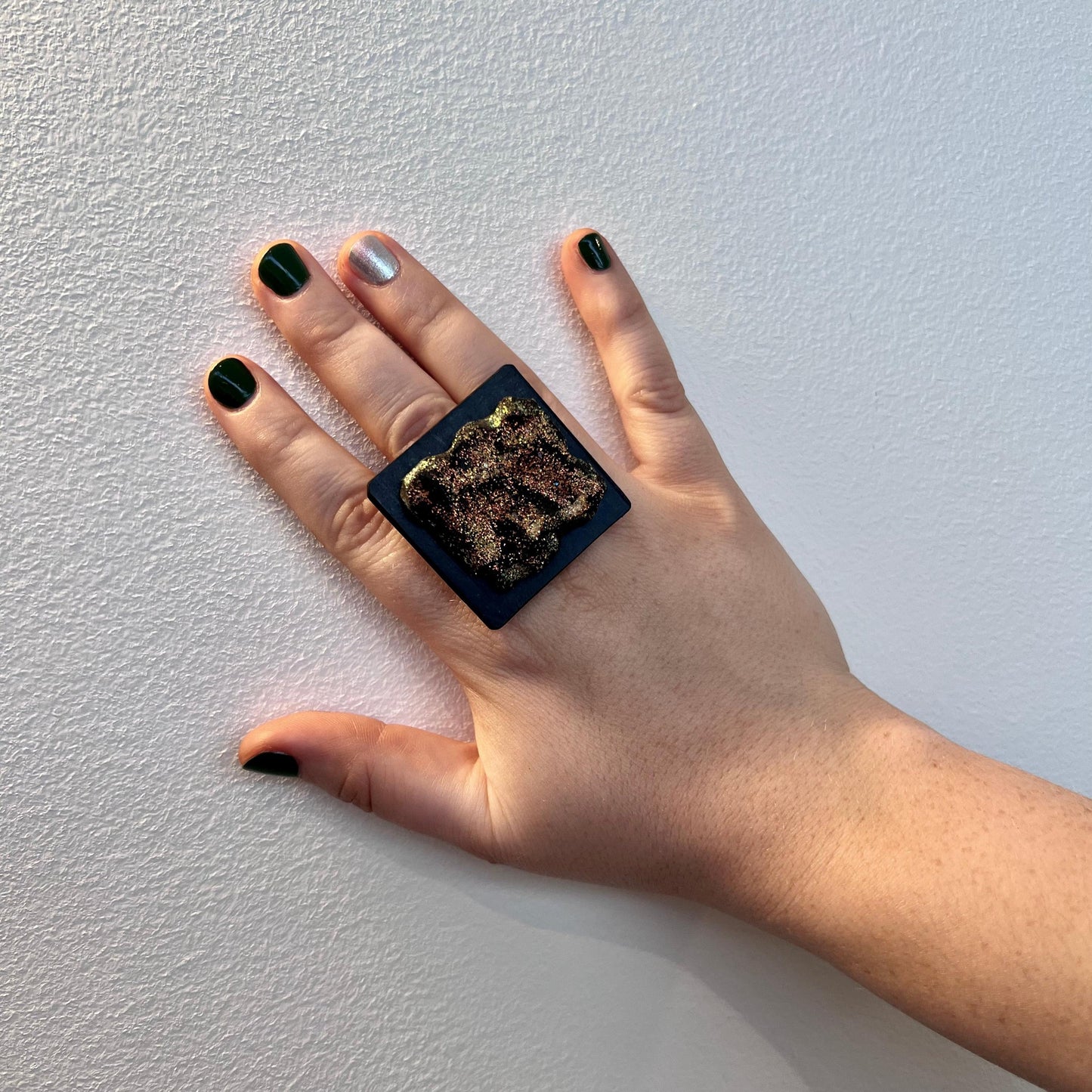 A woman's hand wearing a large rubber black and painted glitter ring