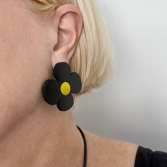 A woman wears a black rubber earring shaped like a Mary Quant daisy flower