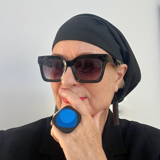 Person wearing a black headscarf and sunglasses, wearing a blue ring.