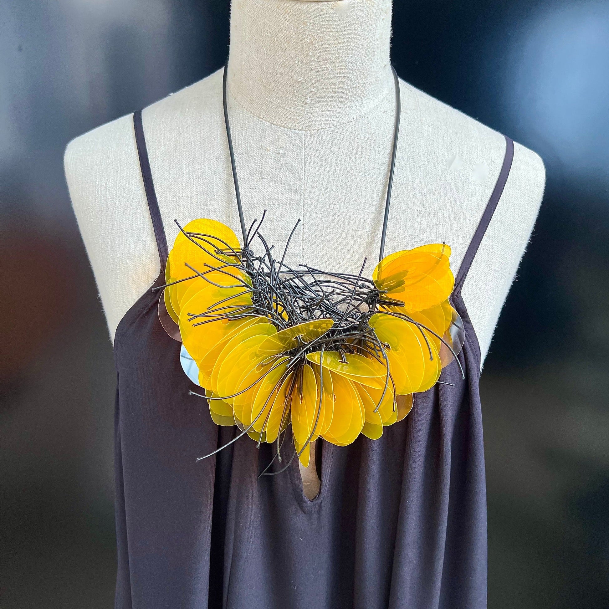 A mannequin wears a necklace made of dozens of clear plastic yellow gold discs on a strand of rubber