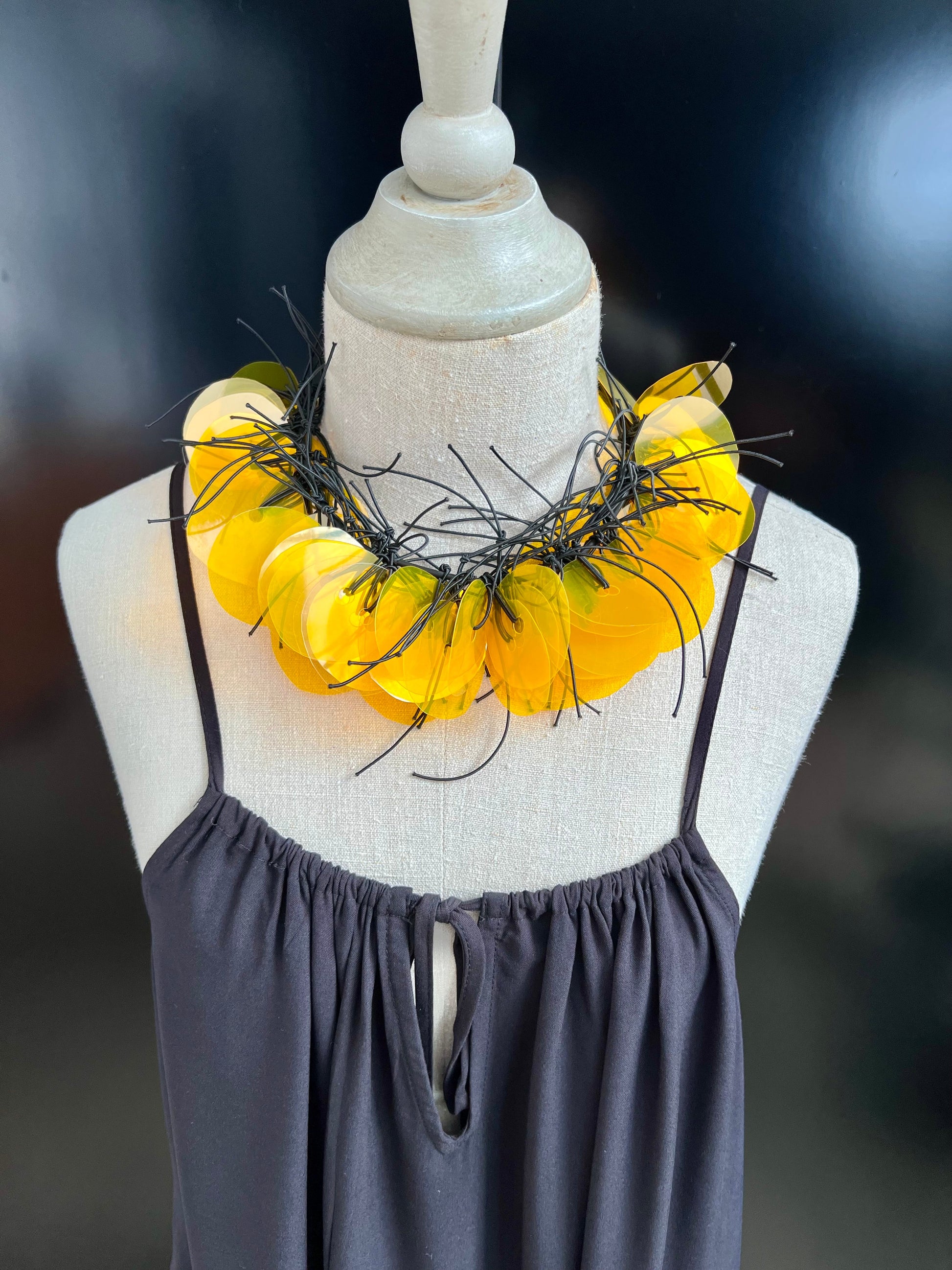 A mannequin wears a necklace made of dozens of clear plastic yellow gold discs on a strand of rubber