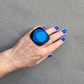 Hand wearing a black and blue ring against a gray background