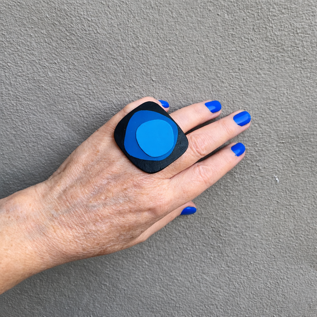 Hand wearing a black and blue ring against a gray background