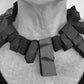 A woman wears a large rectangular shaped choker of black rubber