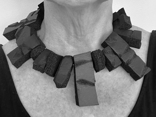 A woman wears a large rectangular shaped choker of black rubber
