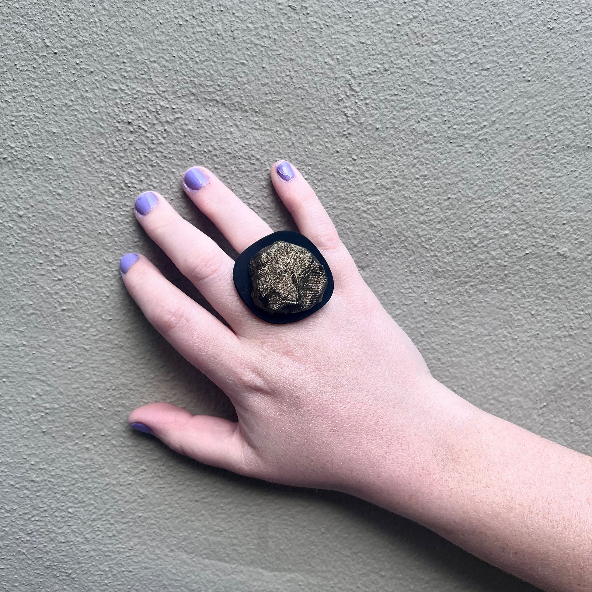 A hand wears a black ring topped with a bronze centre