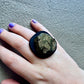 A hand wears a black ring topped with a bronze centre