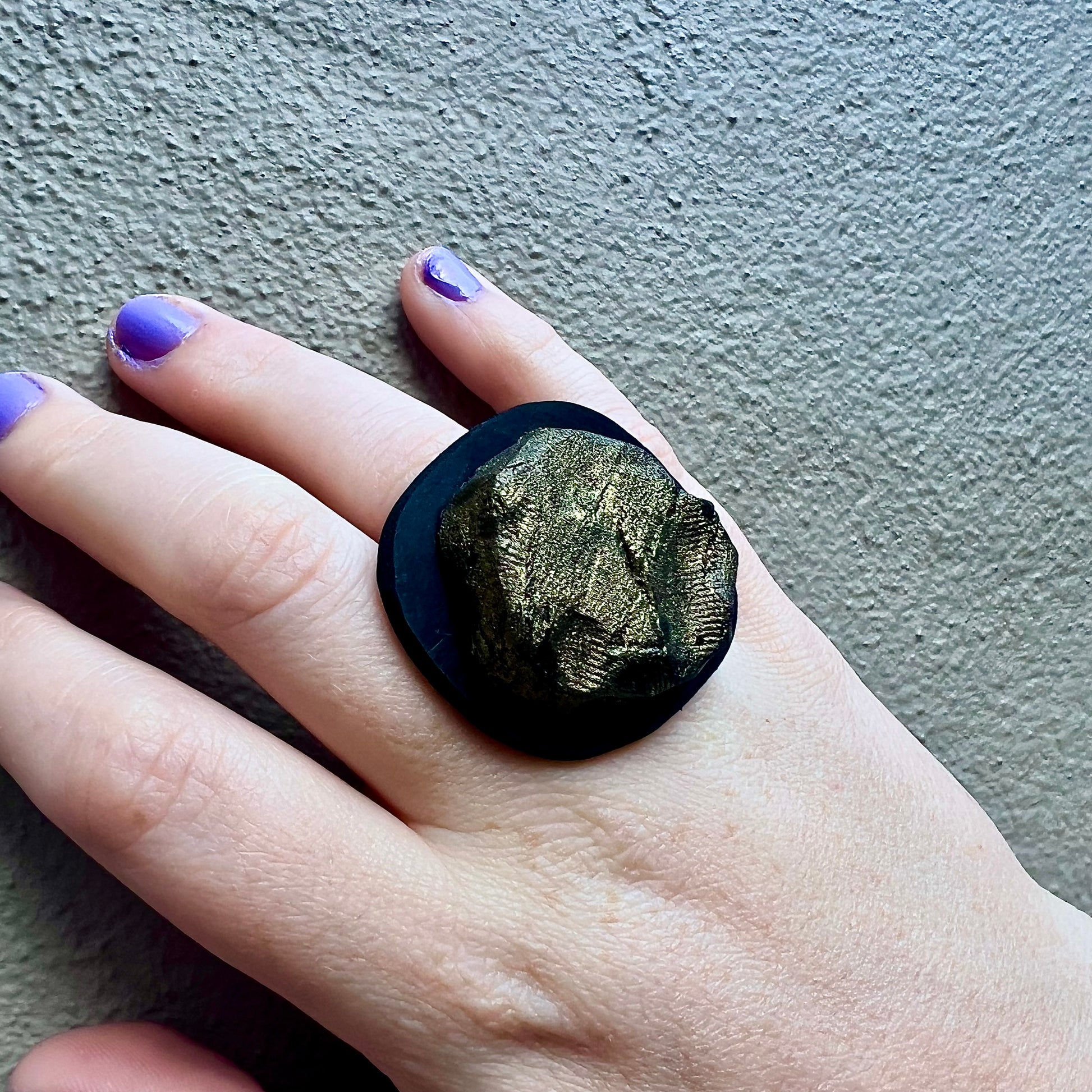 A hand wears a black ring topped with a bronze centre