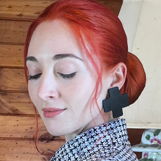A woman wears a pair of black rubber cross stud earrings