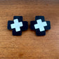 Pair of black earrings with white crosses on a wooden surface