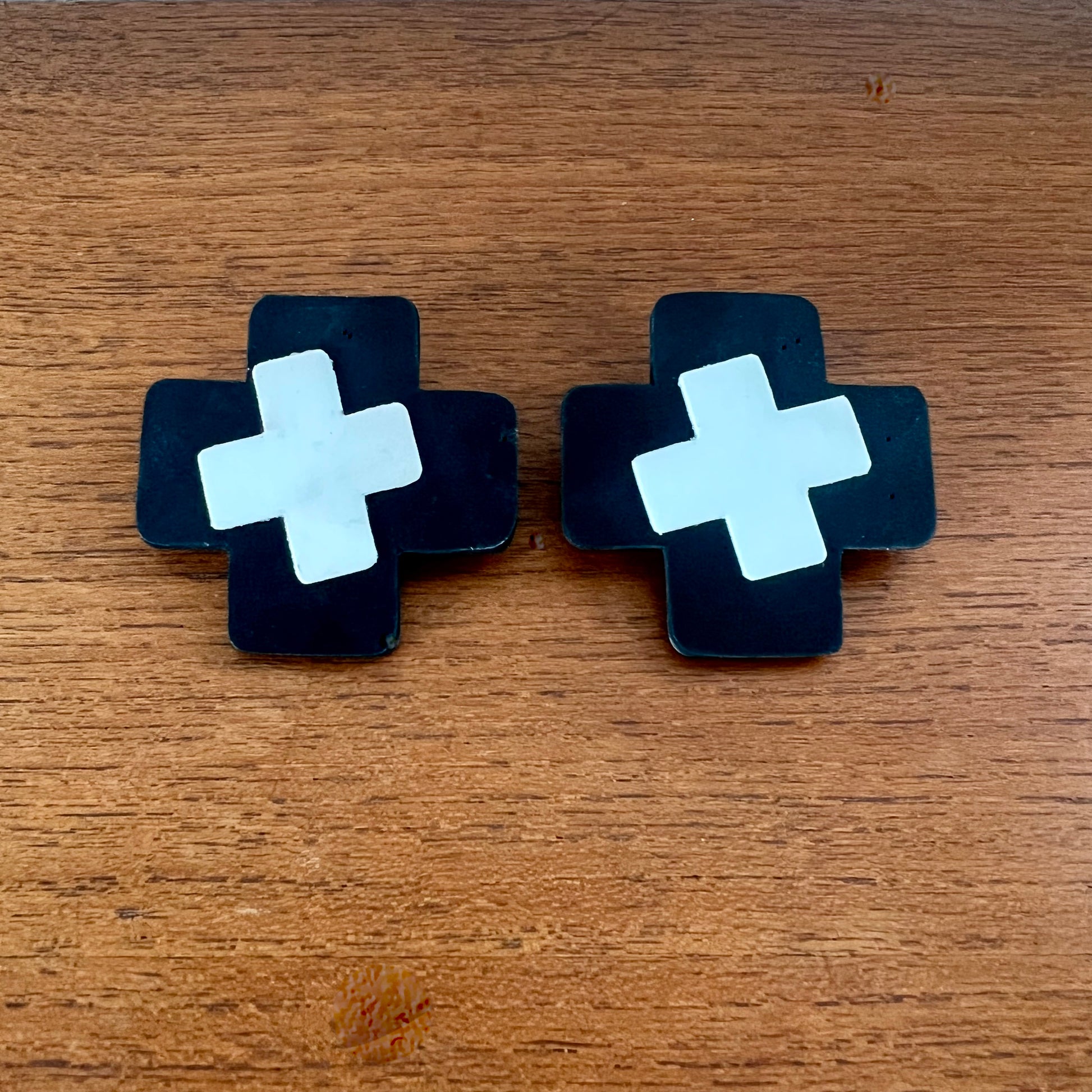 Pair of black earrings with white crosses on a wooden surface