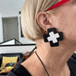 Person wearing black earrings with white crosses in a room setting