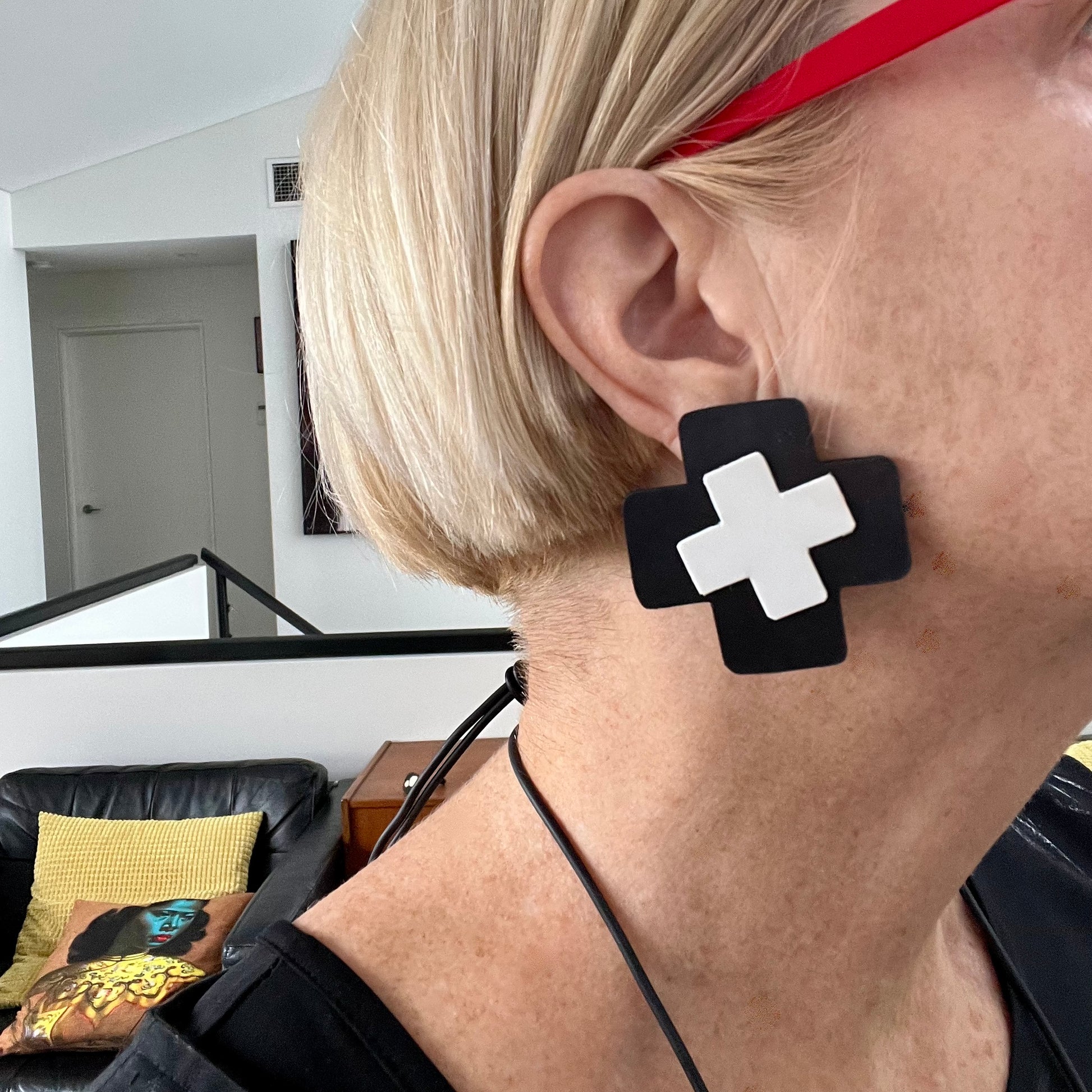 Person wearing black earrings with white crosses in a room setting