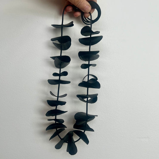 Black leaf-shaped necklace held by a hand against a white background