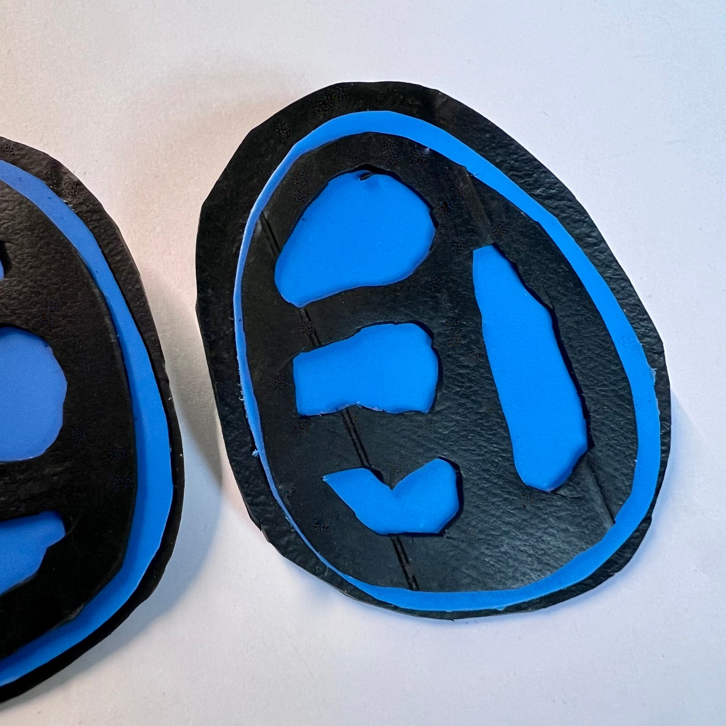 A pair of rubber and plastic blue stud earrings with fossil like cut outs in close up