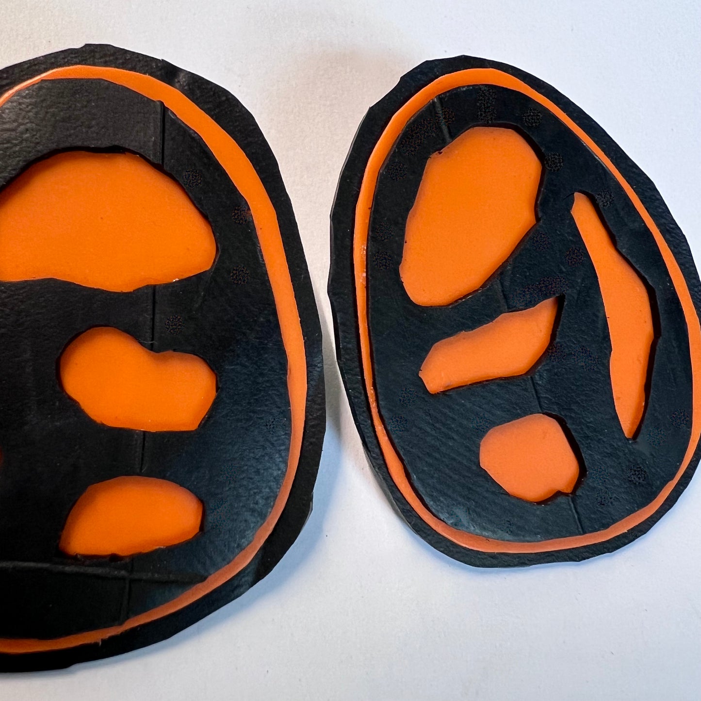 A pair of rubber and plastic orange stud earrings with fossil like cut outs in close up