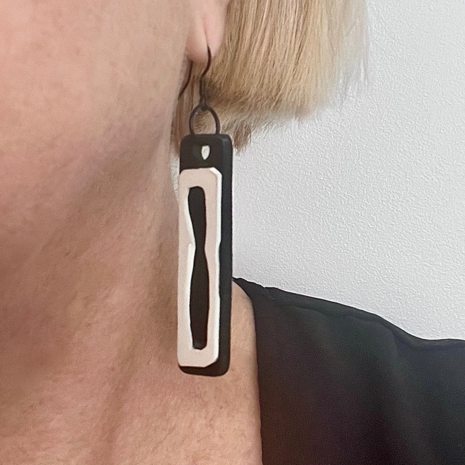 A woman wears a long black and white earring made from rubber