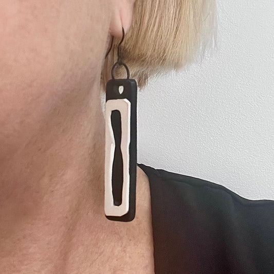 A woman wears a long black and white earring made from rubber