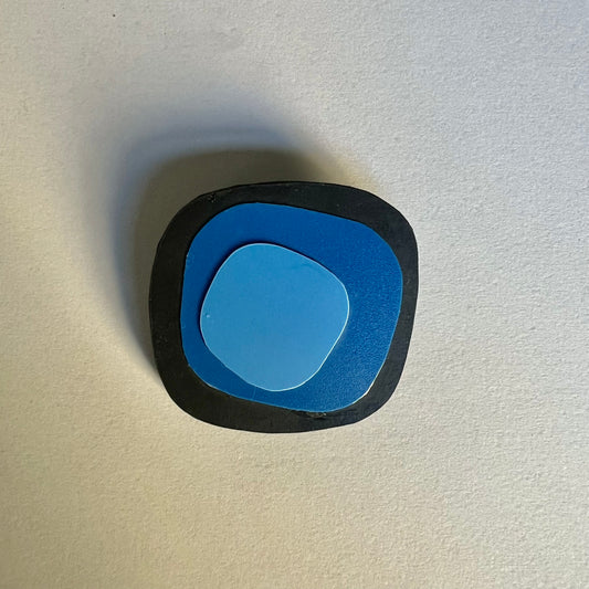 An irregular shaped black brooch base with 2 layers of blue shapes on top