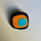A brooch with an irregular shaped black base topped with layers of orange and blue