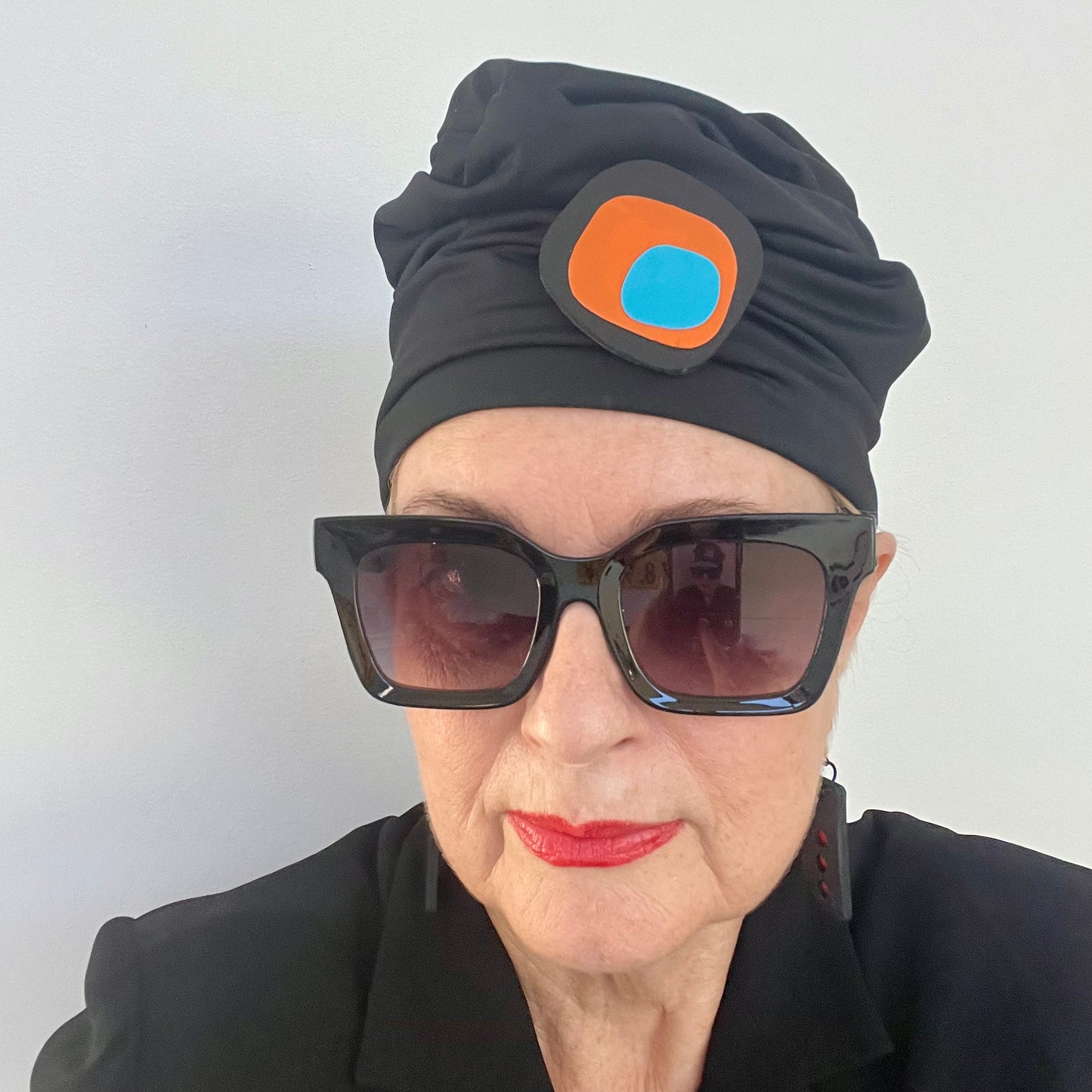 Person wearing a black turban with A brooch with an irregular shaped black base topped with layers of orange and blue