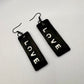 Black rectangular earrings with 'LOVE' text on a light gray background