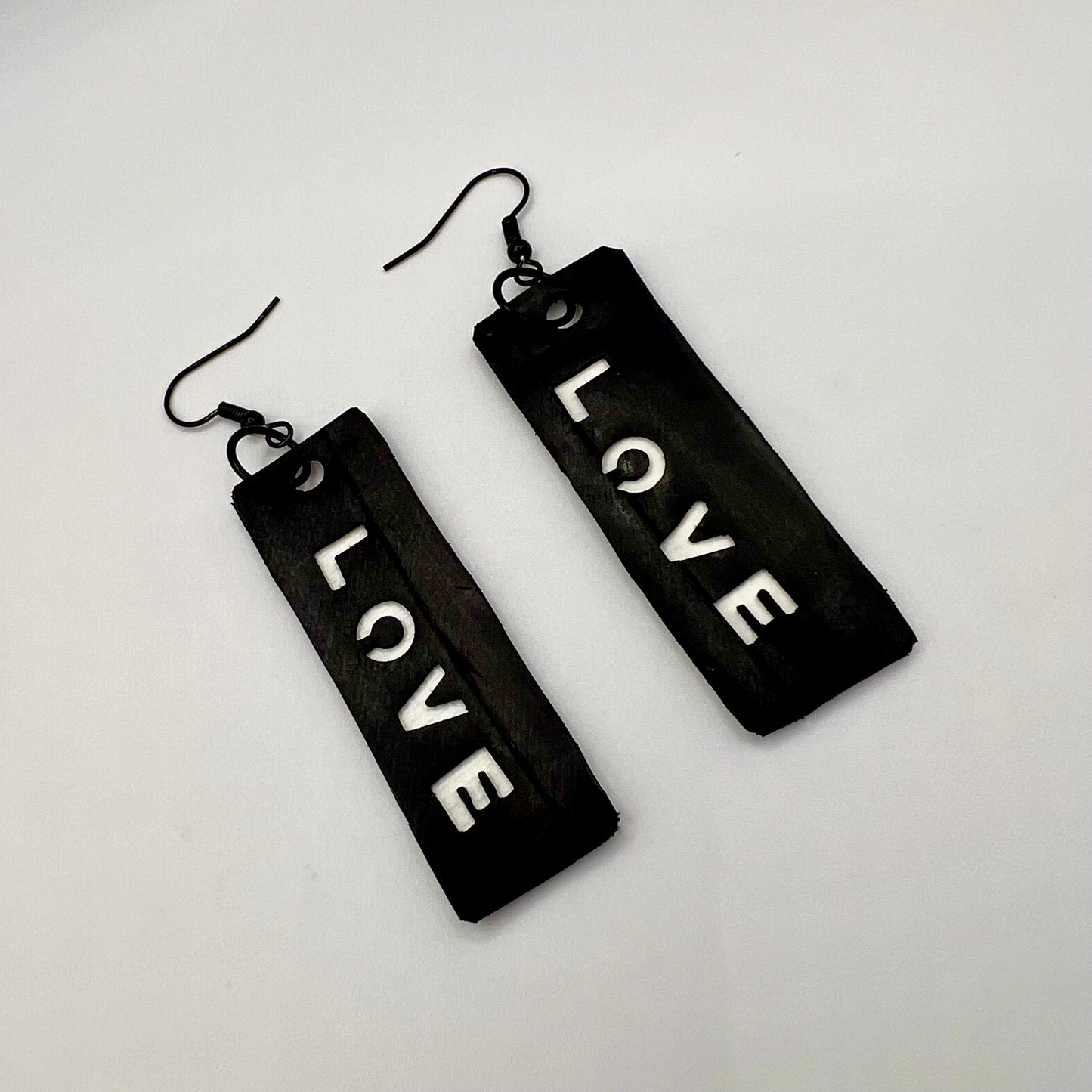 Black rectangular earrings with 'LOVE' text on a light gray background