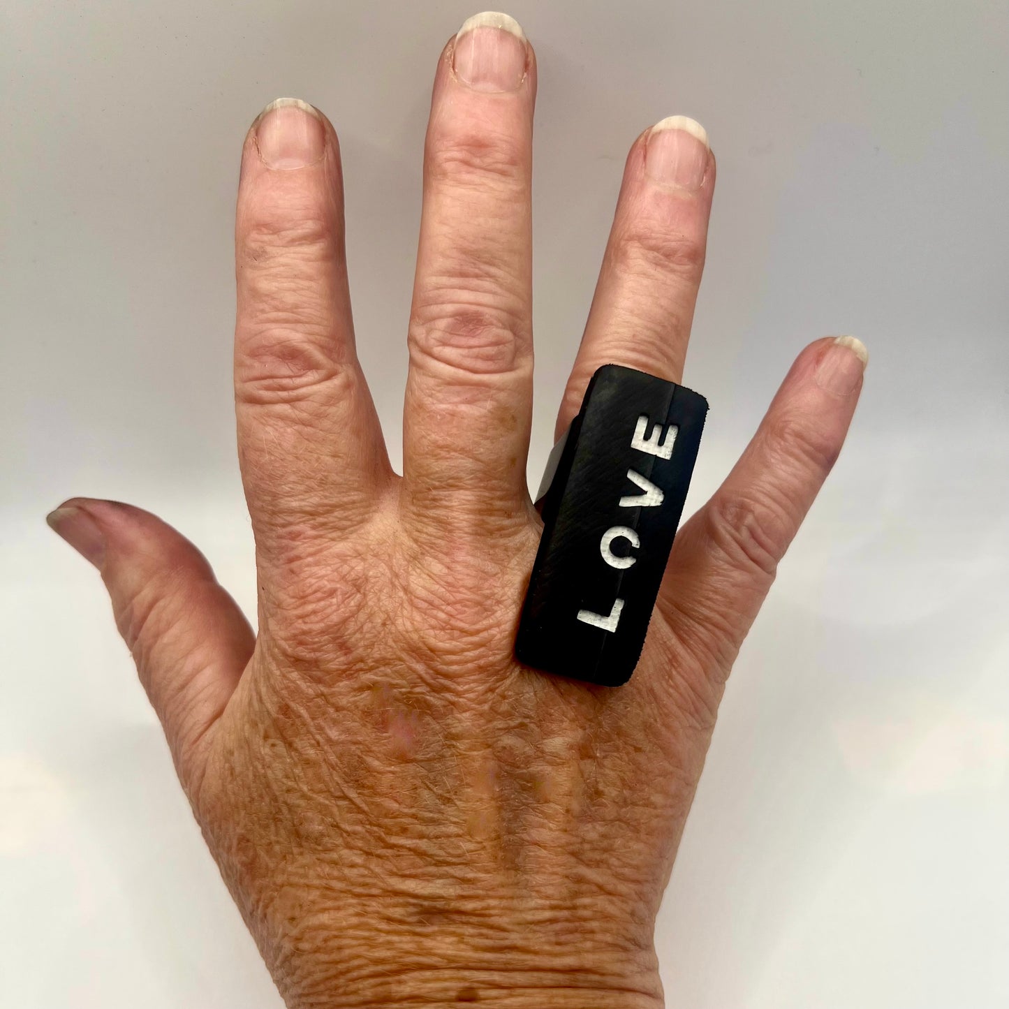 Hand wearing a black ring with 'LOVE' on a neutral background