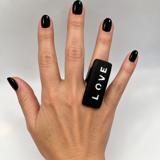A woman's hand wears a long ring with LOVE written on it