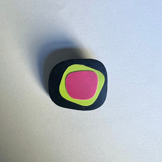 A black irregular shaped brooch layered with green and pink segments