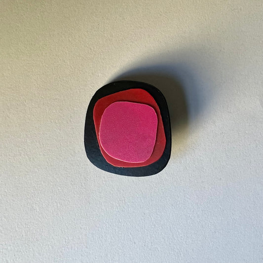 A black irregular shaped brooch topped with layers of red and pink