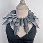 Mannequin wearing a large, leaf-like silver necklace against a plain background
