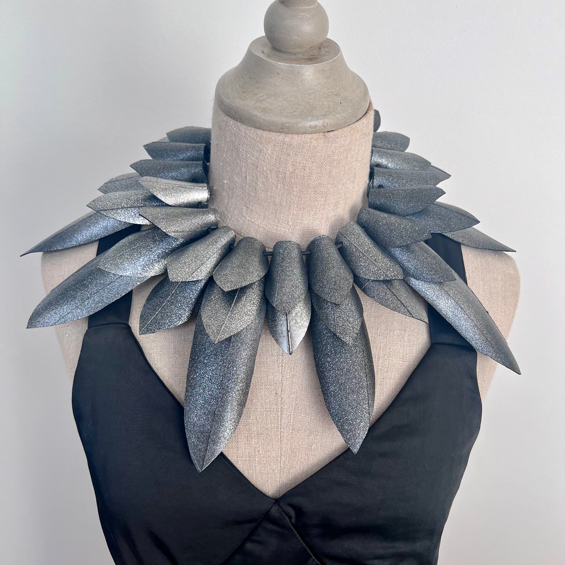 Mannequin wearing a large, leaf-like silver necklace against a plain background