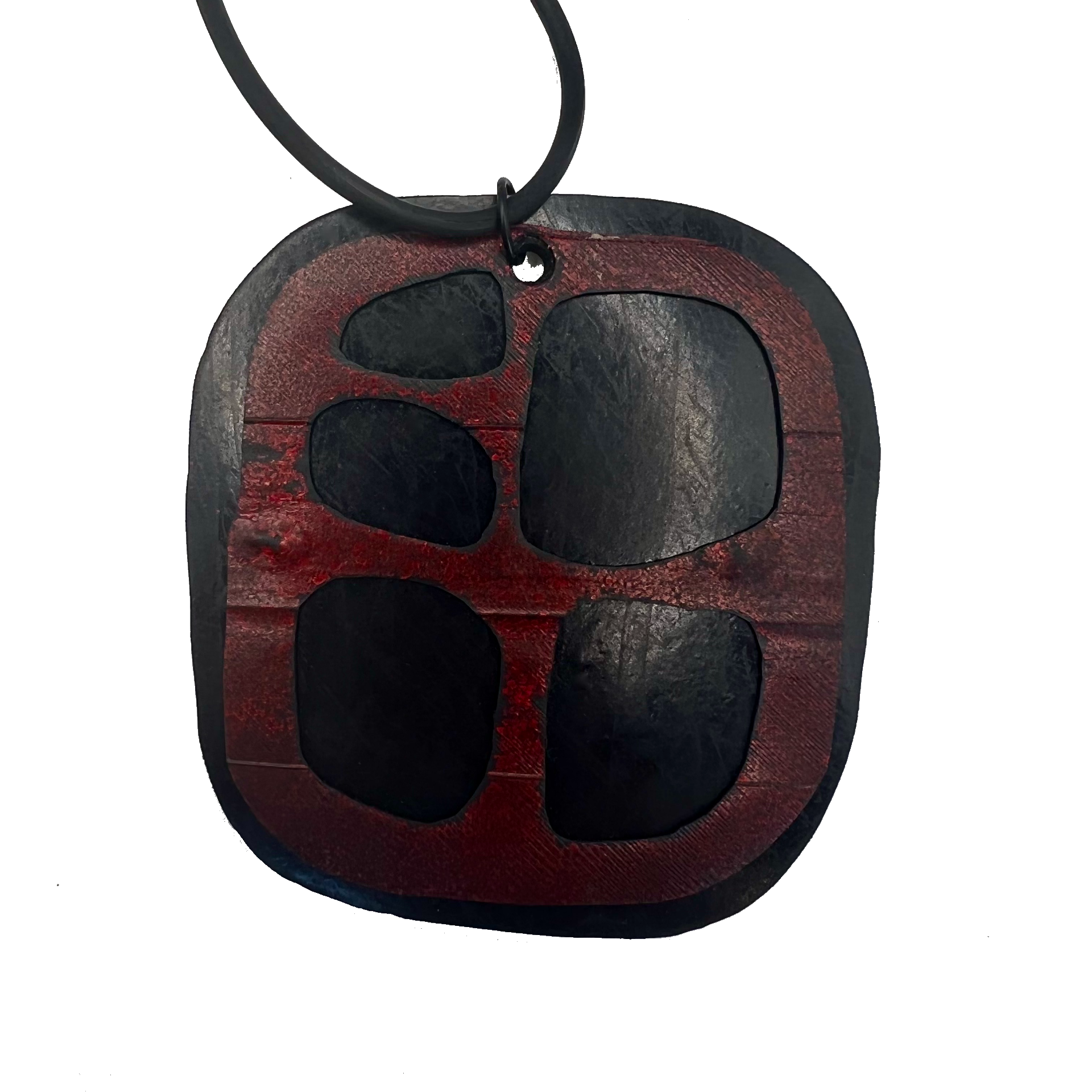 A misshapen square pendant made from black rubber is topped with a red rubber layer that has cutouts