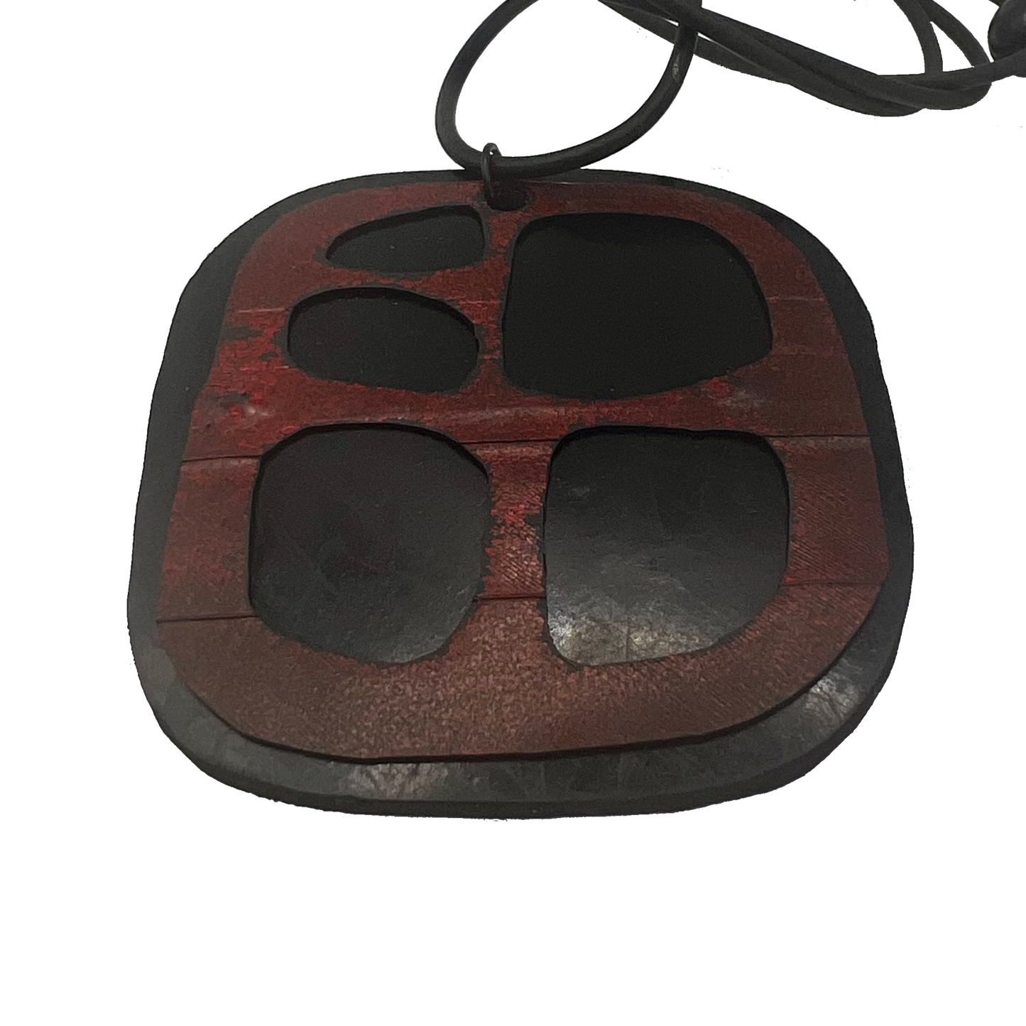 A misshapen square pendant made from black rubber is topped with a red rubber layer that has cutouts on an angle