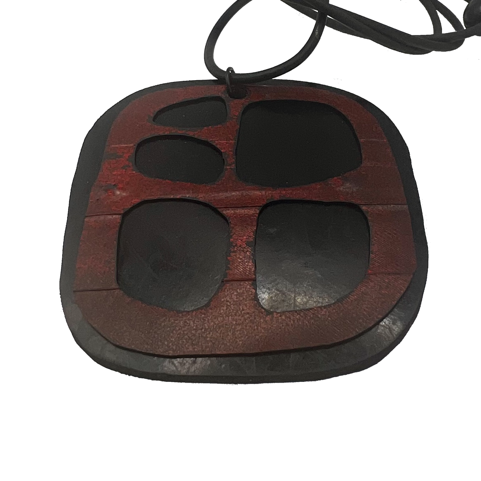 A misshapen square pendant made from black rubber is topped with a red rubber layer that has cutouts on an angle